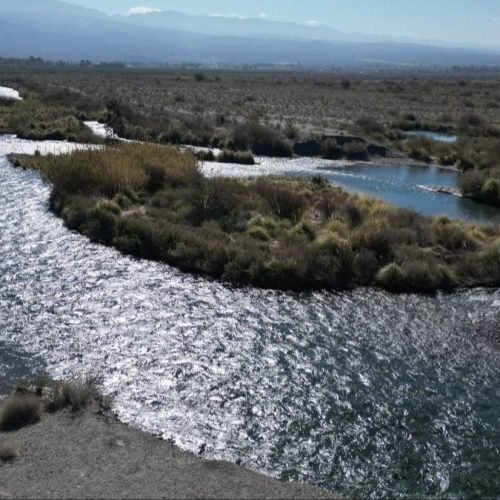 Río de aguas claras que serpentea entre la vegetación baja y la costa pedregosa