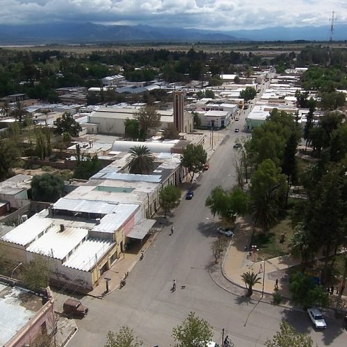 Vista aérea de casas y calles arboladas de una ciudad sanjuanina, con la montaña al fondo